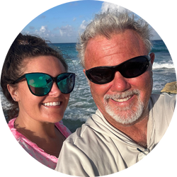 1_55e540 Two people in sunglasses smiling at the beach with ocean in the background.