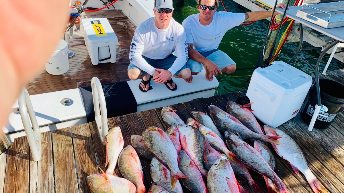 IMG_0243 Two men posing with a large catch of fish on a dock near a boat.