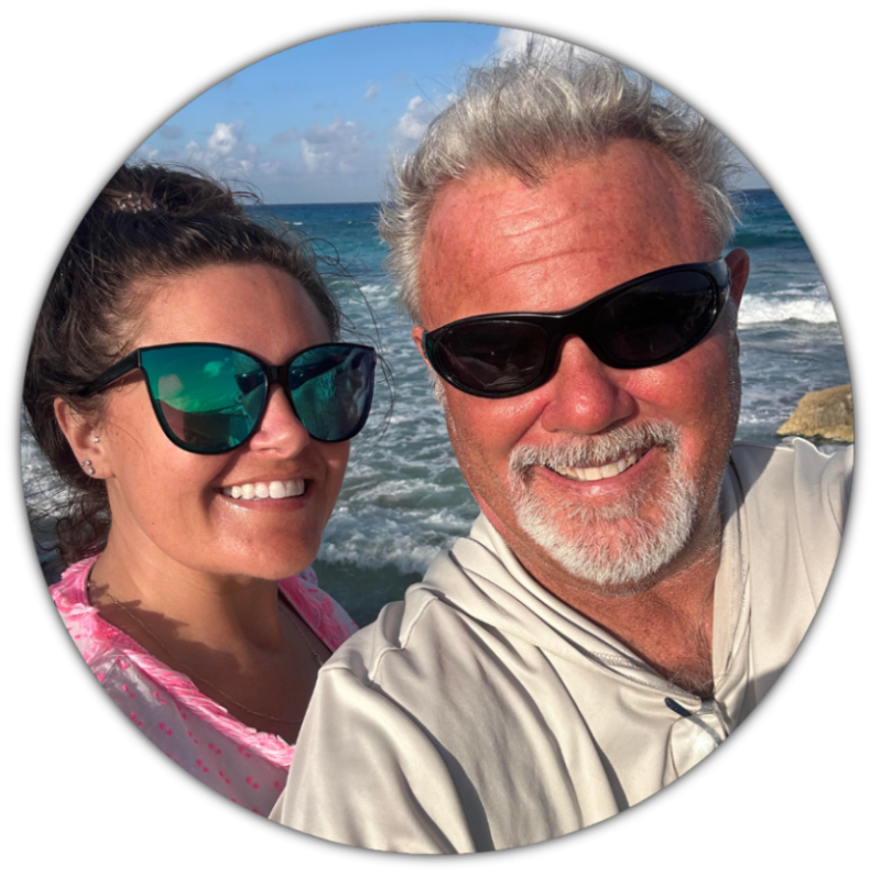 captain glenn new Two adults wearing sunglasses smiling at the beach with ocean in the background.