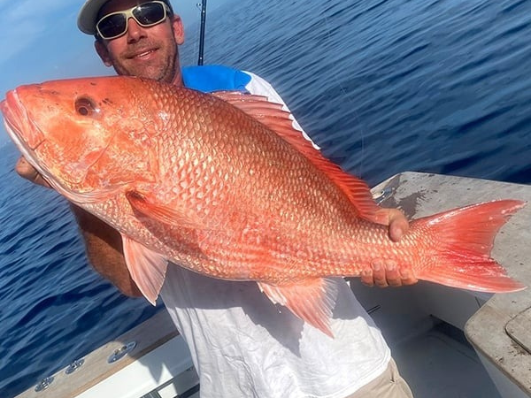 Person on boat holding a large red fish with ocean in background.