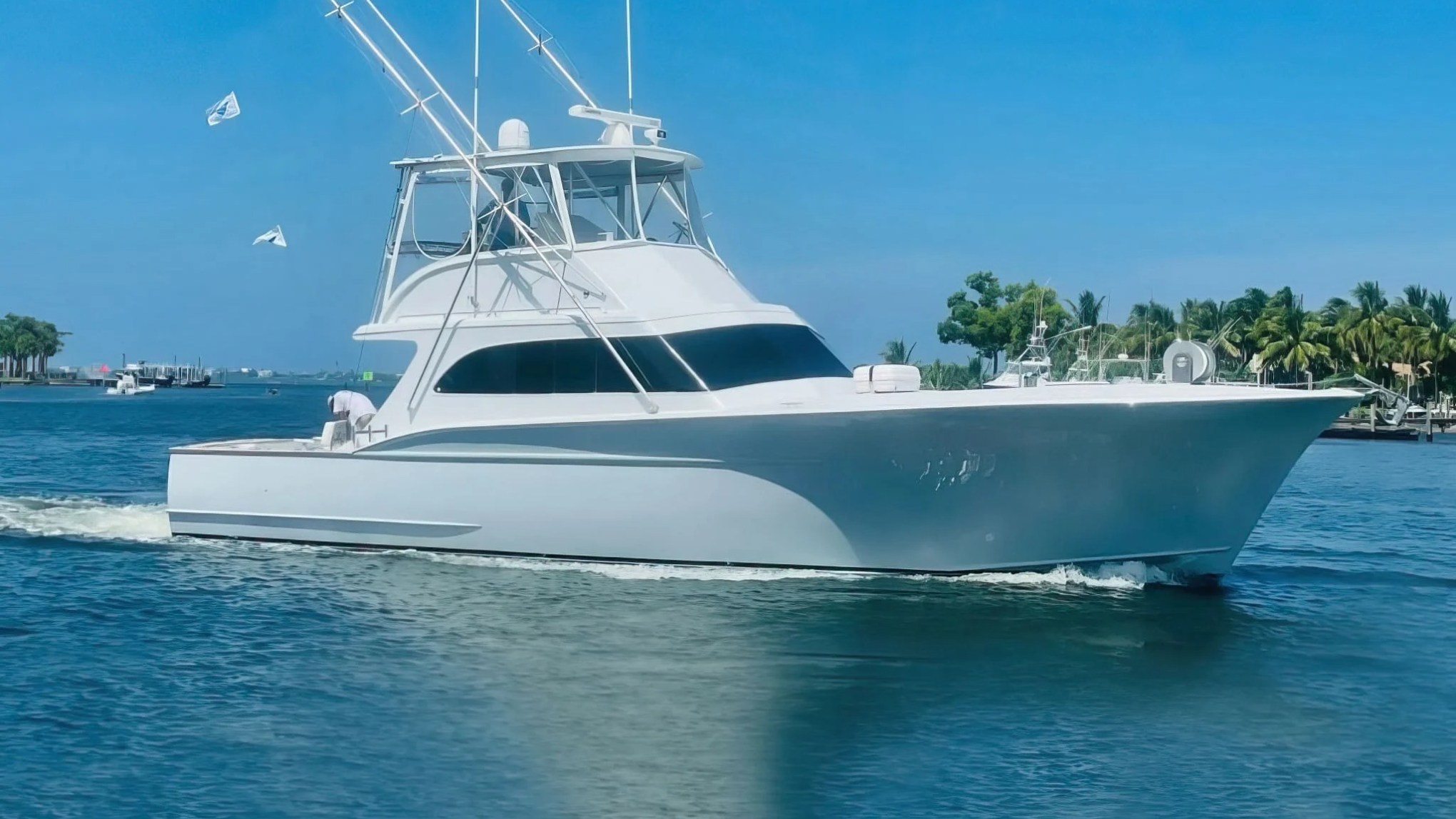 White yacht cruising on a sunny day with clear blue sky and palm trees.