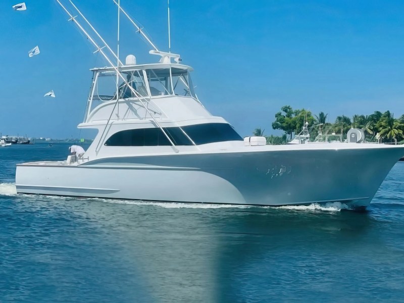 White yacht cruising on a sunny day with clear blue sky and palm trees.
