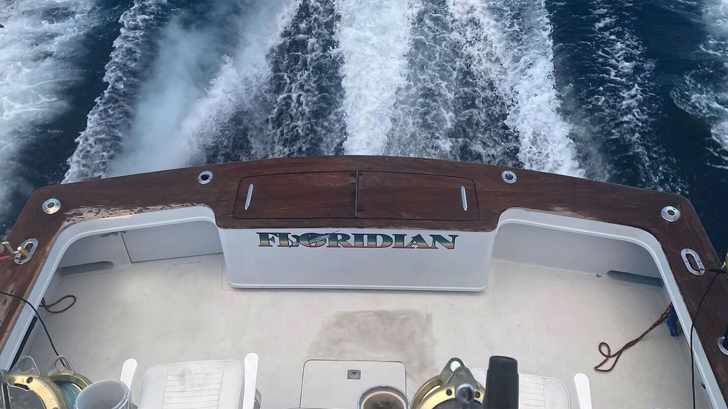 View from boat stern, with fishing rods and ocean wake visible.
