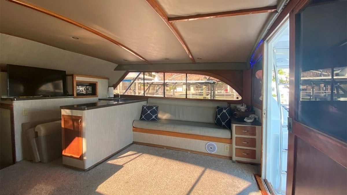 Interior of a boat with a long window, sofa, TV, and open door revealing outside.