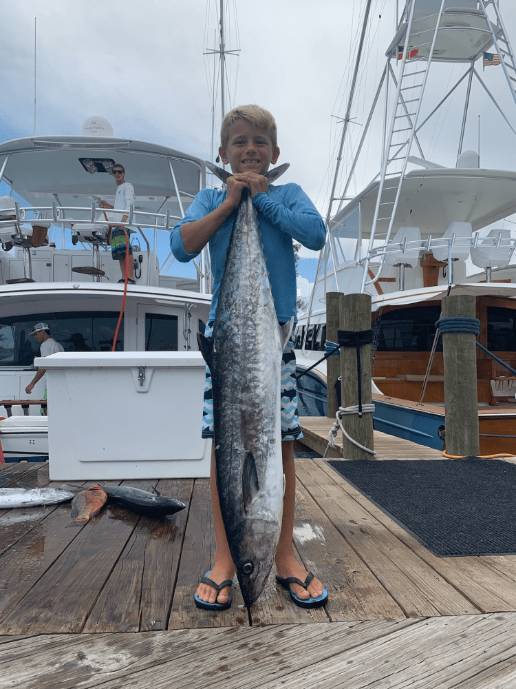 Child holding a large fish on a marina dock, near several boats.