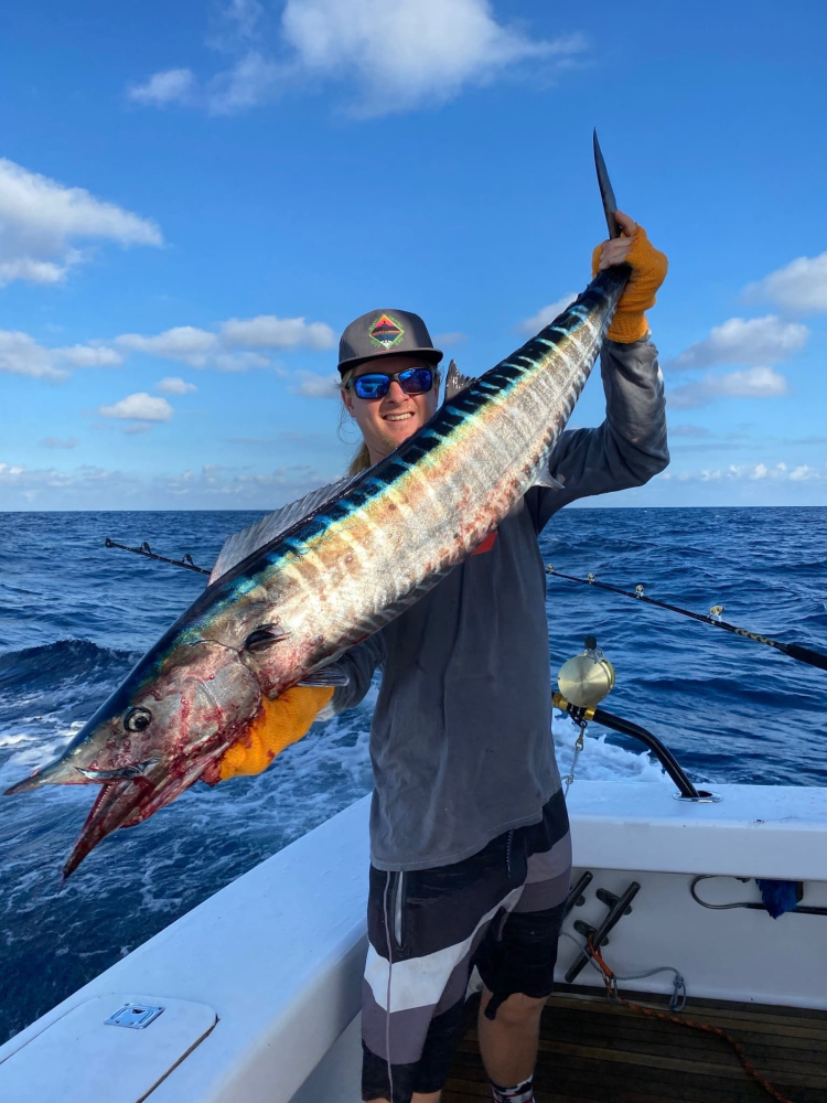 Person on boat holding large fish with ocean in background.