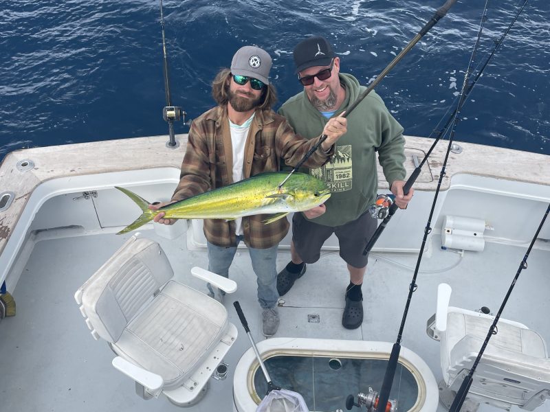 Two people holding a fish on a boat with fishing rods.
