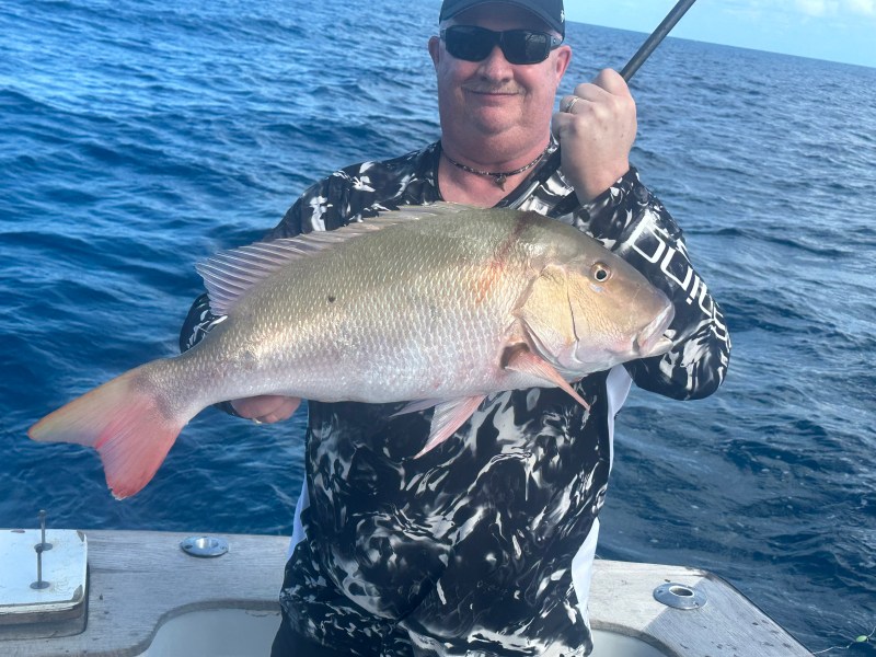 Person holding a large fish on a boat with ocean in the background.