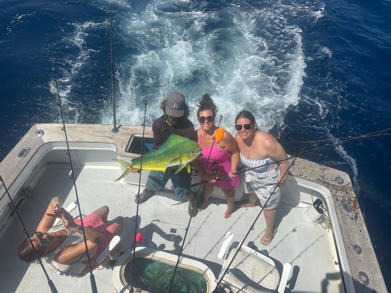 People on a boat display a large fish against the ocean backdrop.