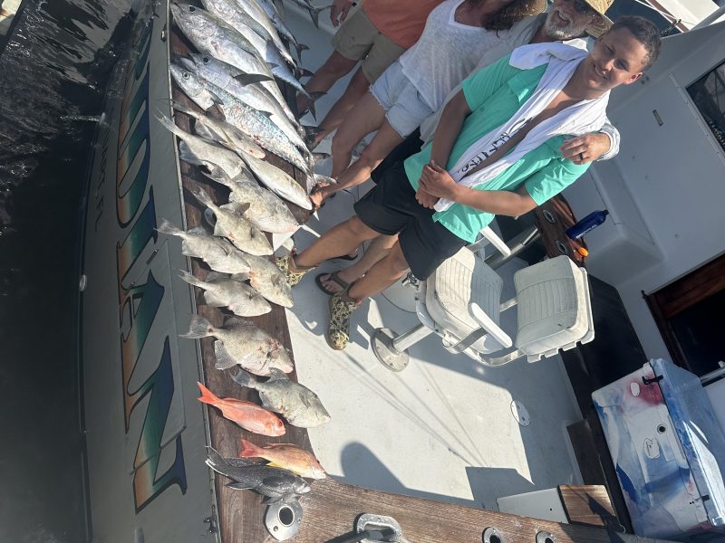 Four people on a boat with a line of caught fish displayed on the railing.